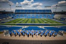 A large group of UK staff members line up at Kroger Field for a photo. 