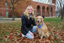 Chalotte Seeger kneeling in the grass with her golden retriever, Honey. 